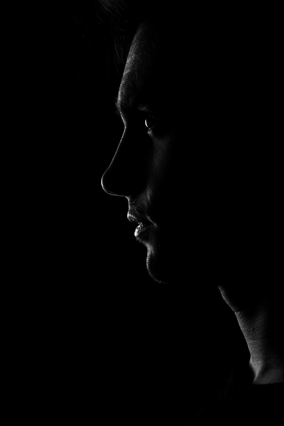 Person's face profile illuminated by side light against dark background.
