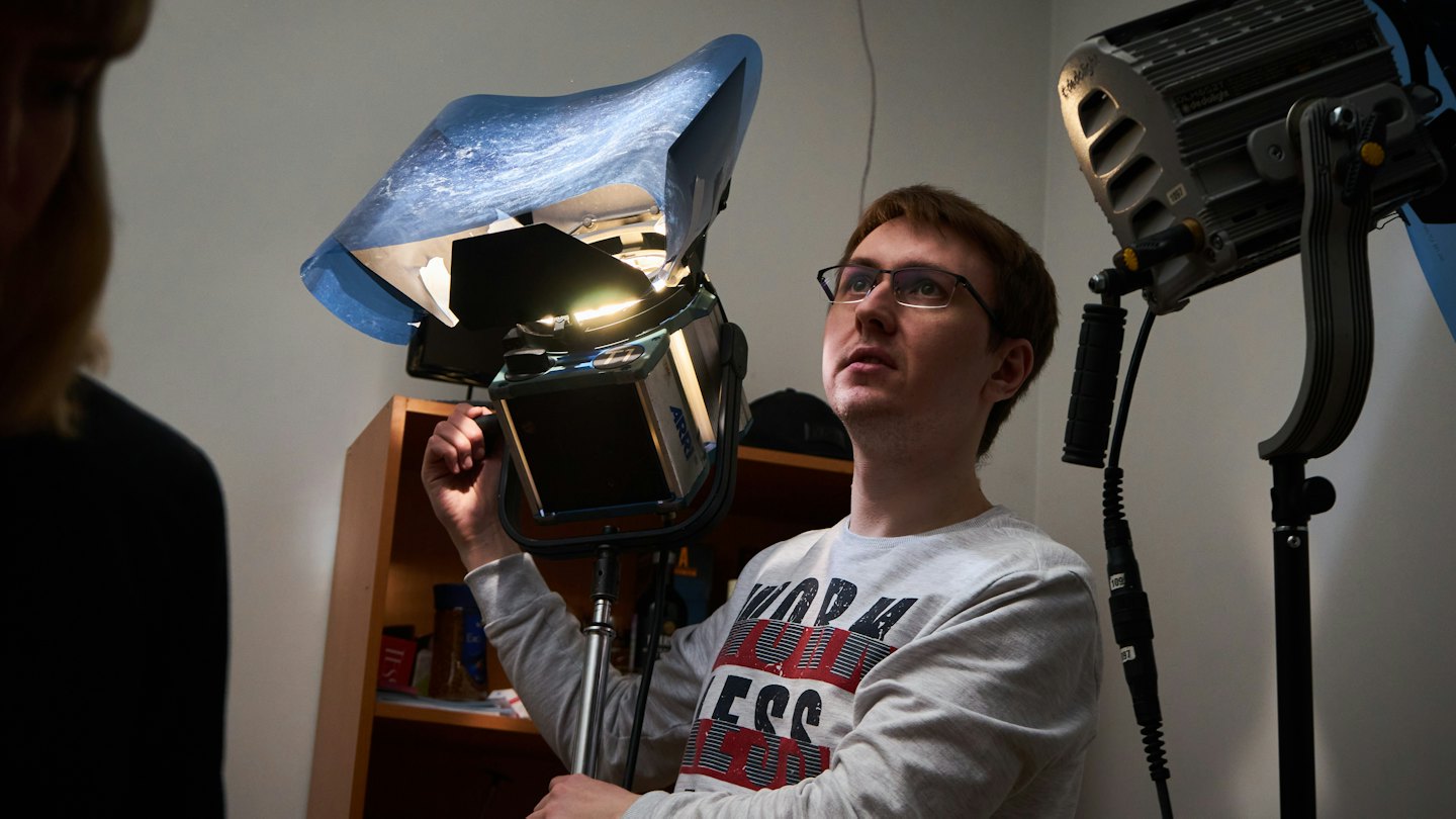 Man in grey sweatshirt adjusts studio light with blue diffuser.