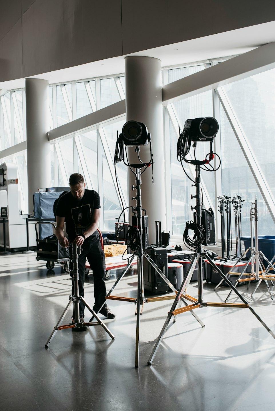 Technician adjusts studio light in modern building with city view.