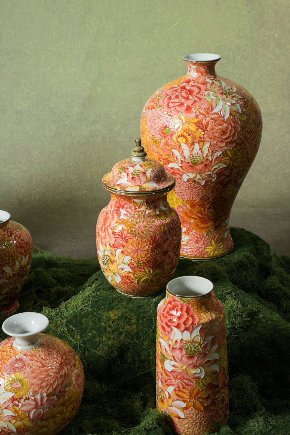 Ceramic vases and jars with floral patterns rest on moss.